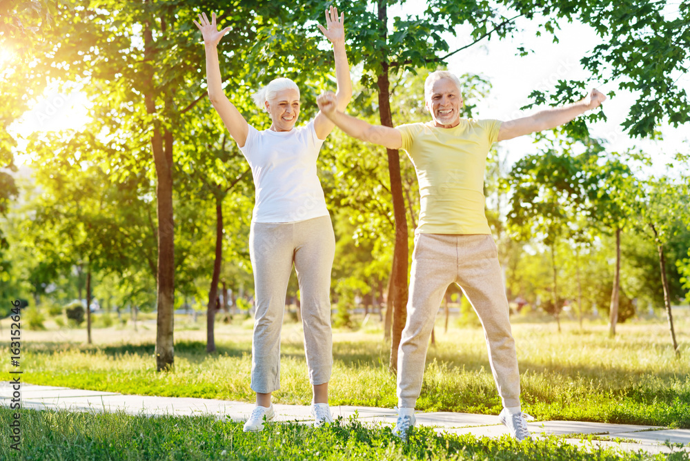 Overjoed aged couple doing sport exercises in the park