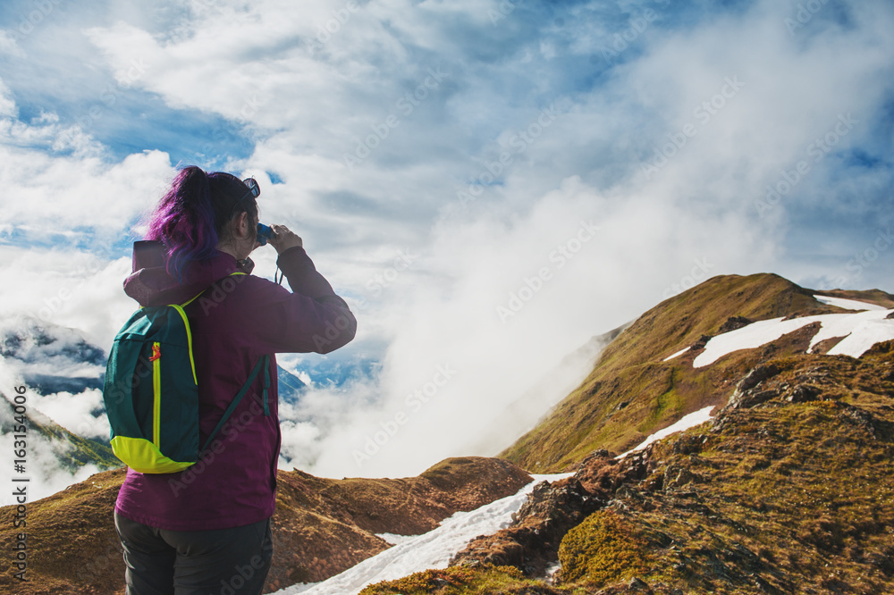 Woman hiker standing on the top of mountain and looking in binoculars Woman hiker standing on the top of mountain and looking in binoculars