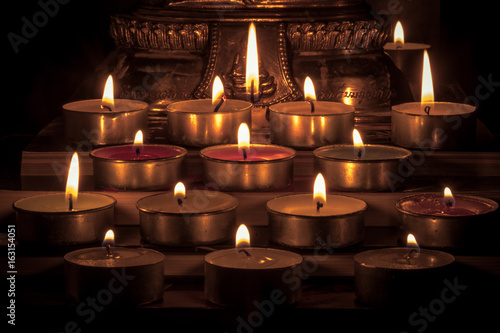 Close Up Group of burning candles in thai style with blurred buddha statue background and concept of peace, meditation and relaxation