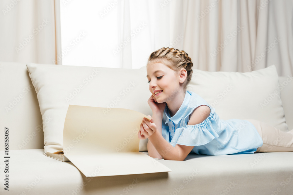 adorable smiling girl reading book while lying on sofa at home adorable smiling girl reading book while lying on sofa at home