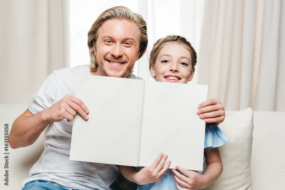 smiling father and daughter holding book while sitting on sofa at home smiling father and daughter holding book while sitting on sofa at home