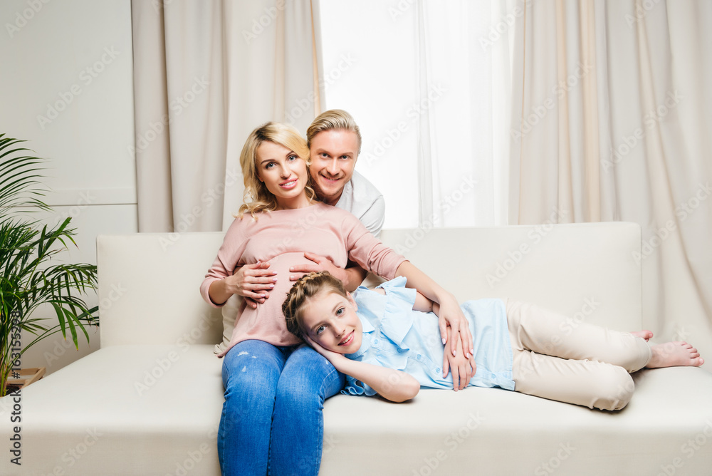 man hugging pregnant woman with little daughter lying on sofa man hugging pregnant woman with little daughter lying on sofa
