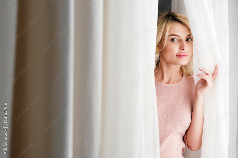 portrait of attractive pensive woman looking out of curtain at home portrait of attractive pensive woman looking out of curtain at home