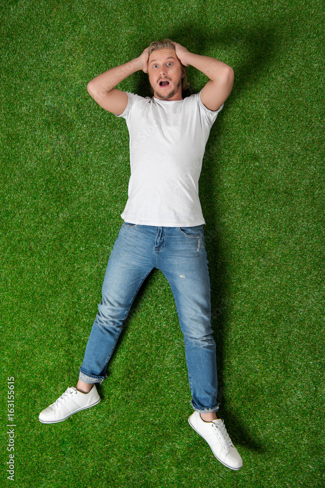 young astonished man with hands on head lying on the meadow young astonished man with hands on head lying on the meadow