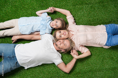above view of happy family looking at camera while lying on the grass