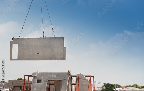 Construction site crane is lifting a precast concrete wall panel.