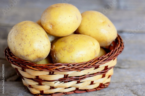 Raw potatoes. Young raw potatoes in a wicker basket isolated on an old wooden background. Closeup