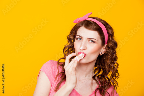 girl in pink dress pinup-style eats cream licks fingers