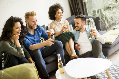 Friends watching TV , drinking cider and having fun in the room