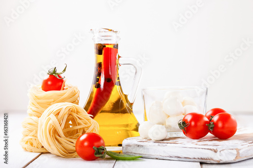 Olive oil with pepper in a bottle, paste, cheese and tomatoes on a light background. Selective focus. Copy space