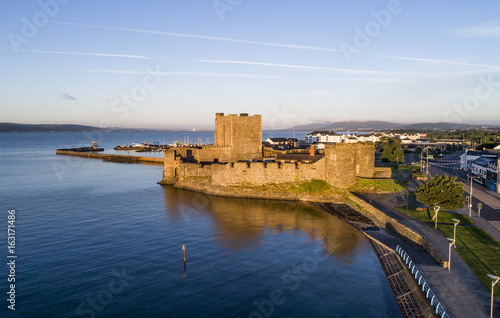 Medieval Norman Castle in Carrickfergus near Belfast, Northern Ireland. Aerial view at sunrise with far view of Belfast in the background.