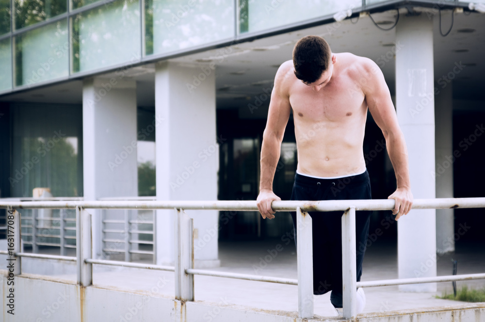 Fototapeta premium Young man warms up with some dips in front of modern sport center.