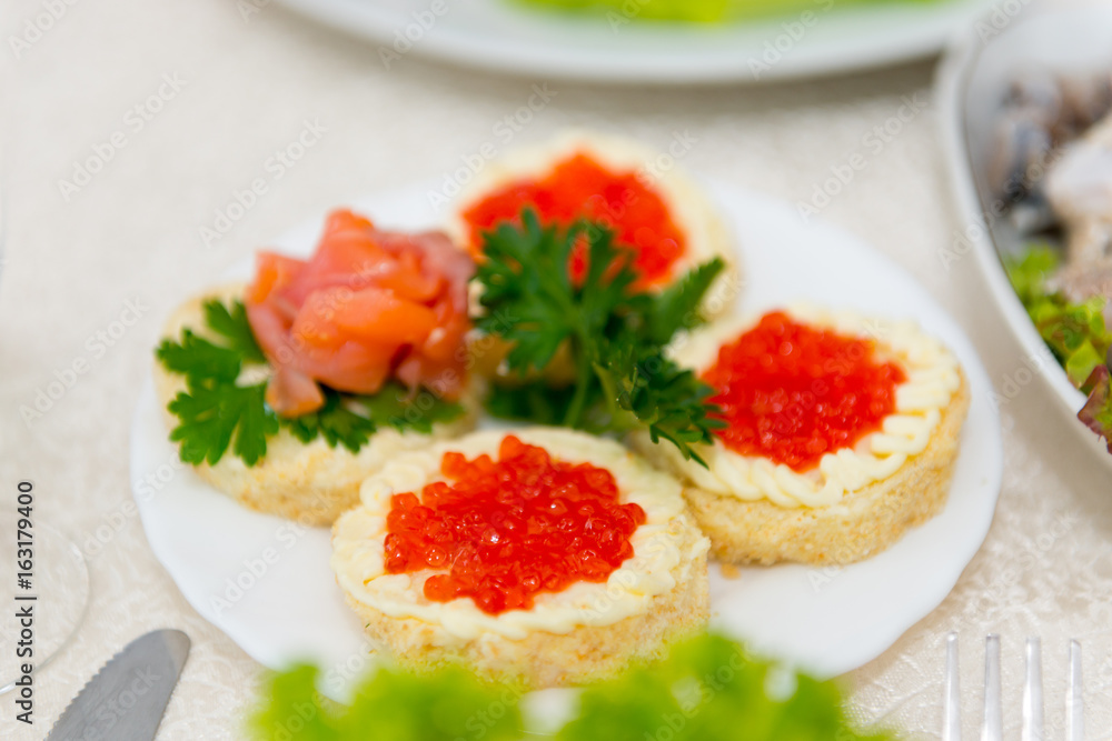 Sandwiches with red caviar and salmon are spread on a plate on a buffet table close up. Sandwiches with red caviar and salmon are spread on a plate on a buffet table close up.