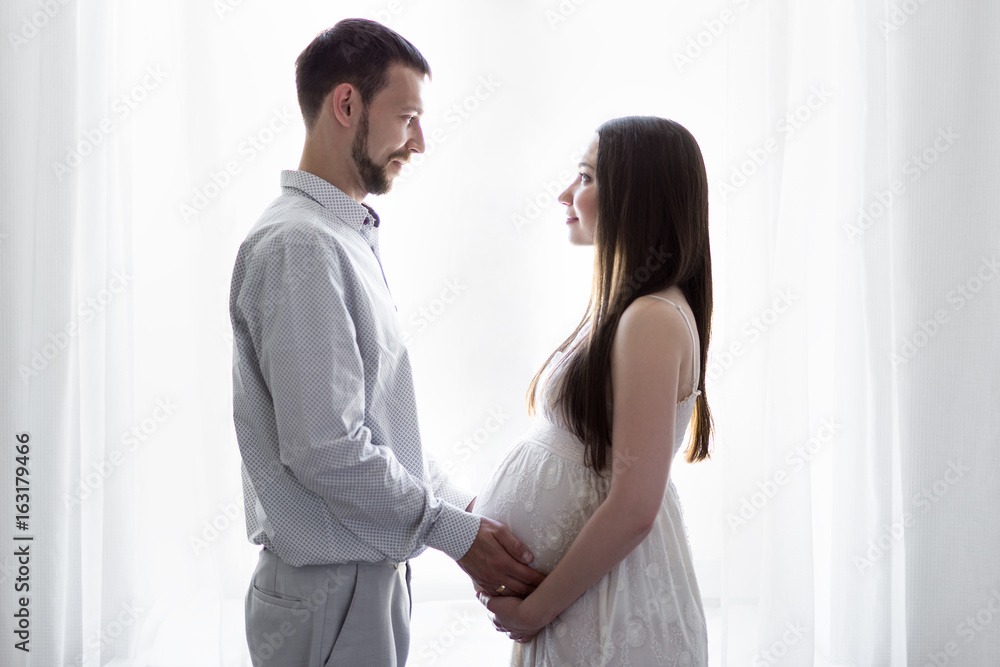 family, pregnancy and parenthood concept - happy pregnant couple in front of the window family, pregnancy and parenthood concept - happy pregnant couple in front of the window