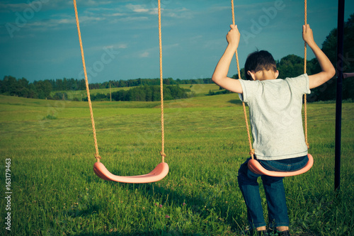 Foto Sad lonely boy sitting on swing