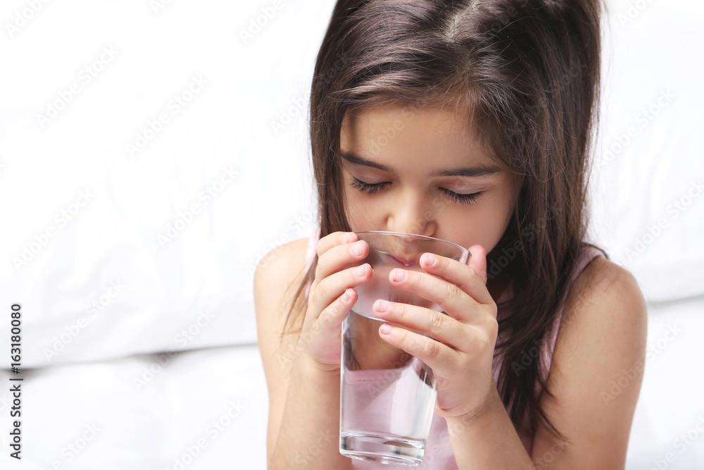 Beautiful little girl drinking water on white bed Beautiful little girl drinking water on white bed