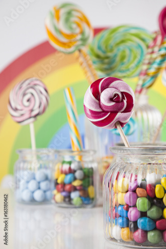 Colorful candies in jars on table on wooden background