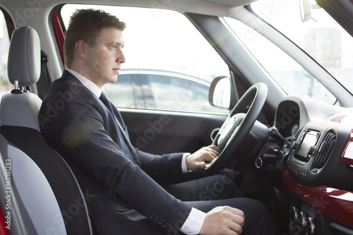 Businessman sitting in his car in a highway jam. Looking in the distance while in traffic. Suit and tie businessman sitting in his automobile.