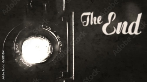 Retrograded animation: a vintage old fashioned The End title, silent film ariston style, slowly appearing, over the light beam of a Super 8mm projector lens. Antique ghosts, past. Diegetic audio.
 photo