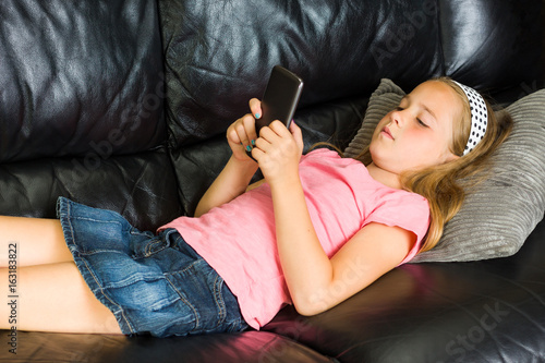 Pretty little girl lying on the couch with smartphone