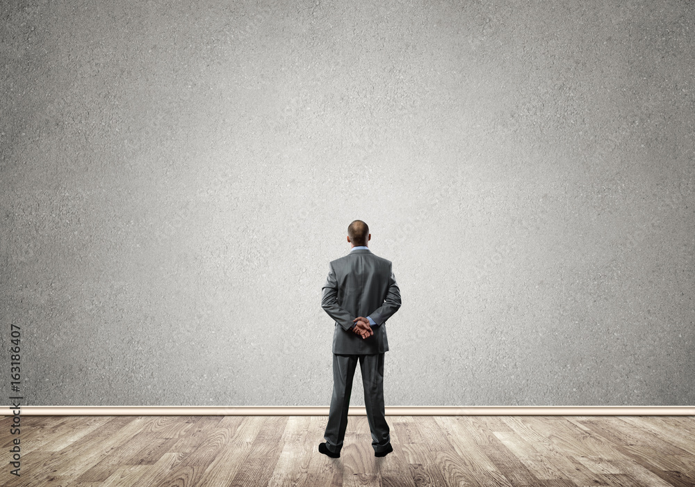 Businessman with hands behind his back and looking at blank concrete wall Businessman with hands behind his back and looking at blank concrete wall