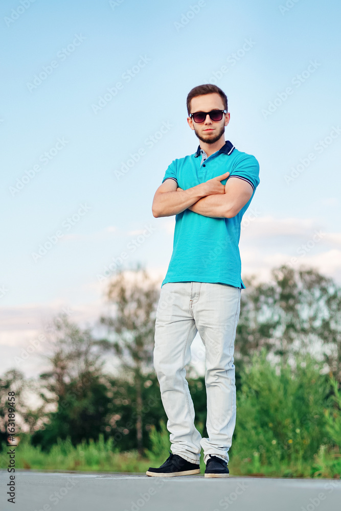 Stylish man with crossed arms wearing blue polo on an empty road