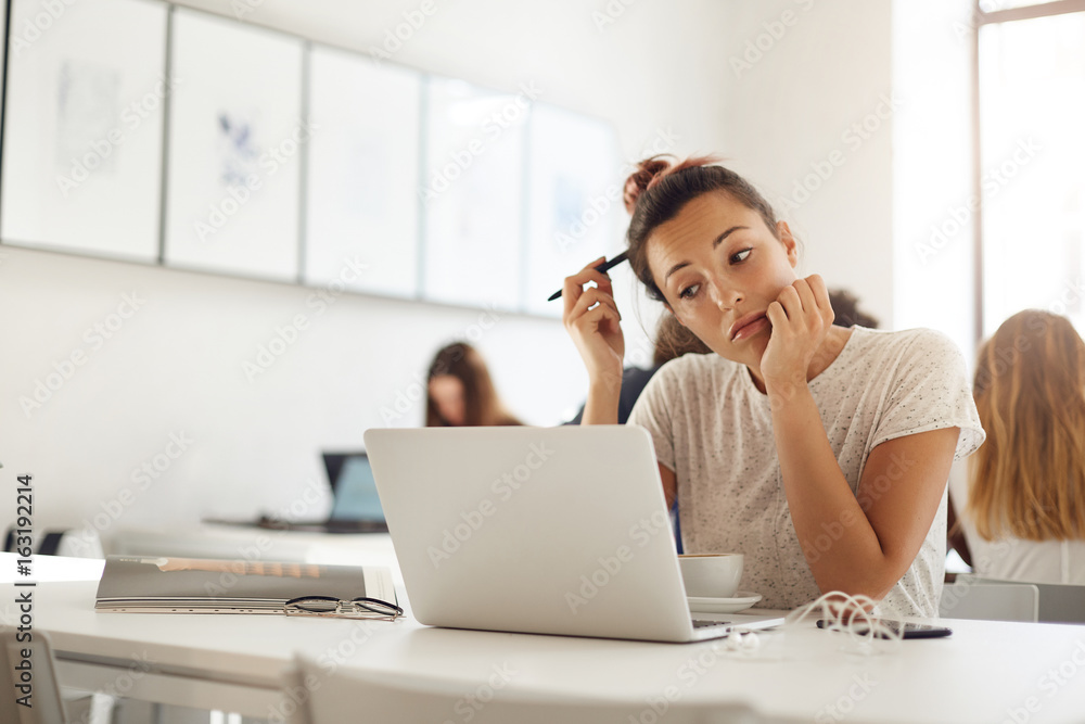 Fashion designer student working on her collection using laptop and a magazine drinking coffee Fashion designer student working on her collection using laptop and a magazine drinking coffee