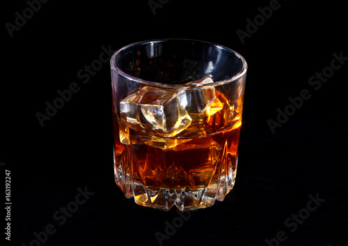 Glass of whiskey or bourbon with ice on black stone table.