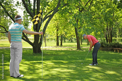 Young men playing golf on course in sunny day