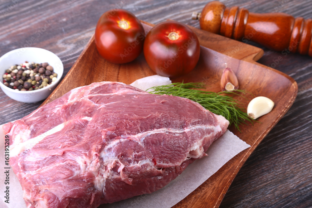 Raw pork steaks on wooden board with herbs, spices, tomatoes and pepper grinder ready for cooking. Selective focus Raw pork steaks on wooden board with herbs, spices, tomatoes and pepper grinder ready for cooking. Selective focus