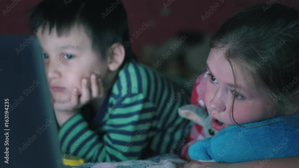 Multi-ethnic boy and white girl lying on the couch watching the notebook in the dark. 4K Multi-ethnic boy and white girl lying on the couch watching the notebook in the dark. 4K