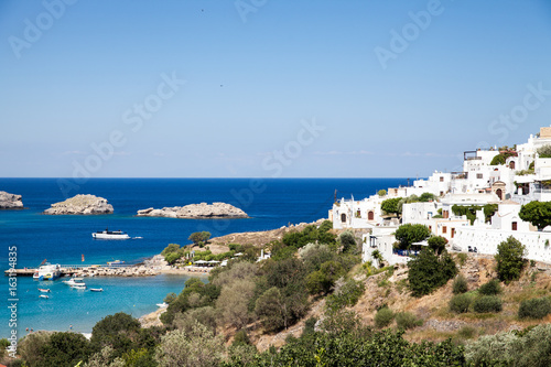 Typical Greek architecture. White houses on the coast. Fragment of the town lidos under acropolis. View of the harbor and bay. Blue sea lagoon and ships.