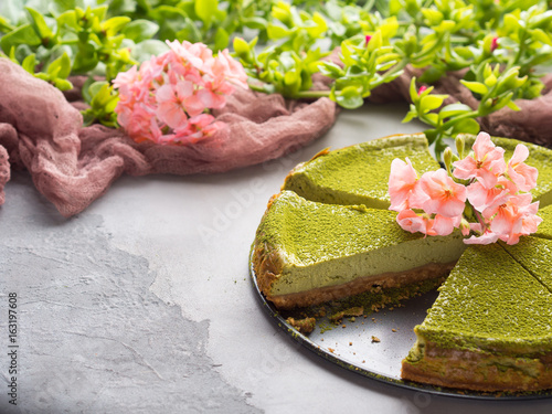Matcha baked cheese cake and pink flowers on gray concrete background