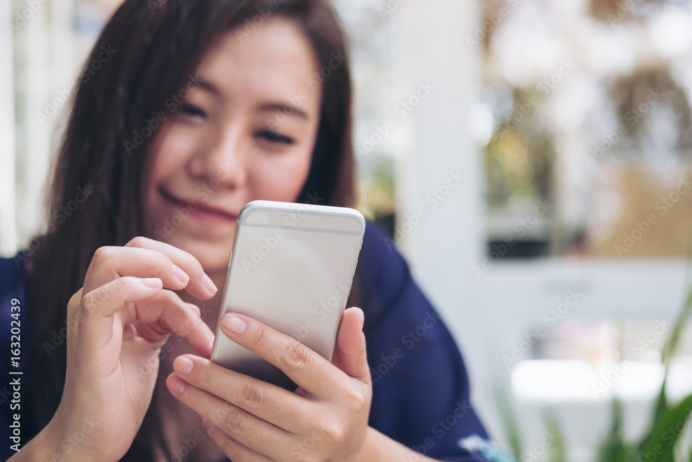 Beautiful Asian woman with smiley face using and looking at smart phone in modern cafe Beautiful Asian woman with smiley face using and looking at smart phone in modern cafe