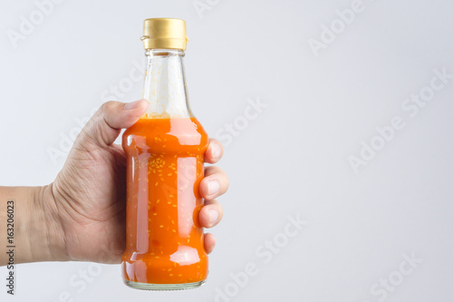 Fototapeta Naklejka Na Ścianę i Meble -  Hand holding spicy red hot sauce in glass bottle for Sukiyaki or hot pot