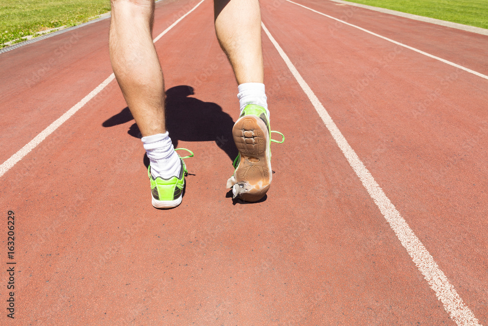 An exhausted athlete on a running track wearing broken green running shoes with big holes in the sole. An exhausted athlete on a running track wearing broken green running shoes with big holes in the sole.