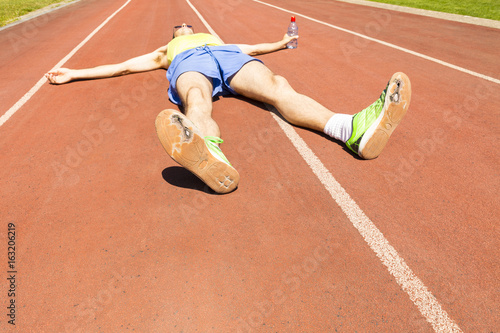 An exhausted athlete on a running track wearing broken green running shoes with big holes in the sole. photo