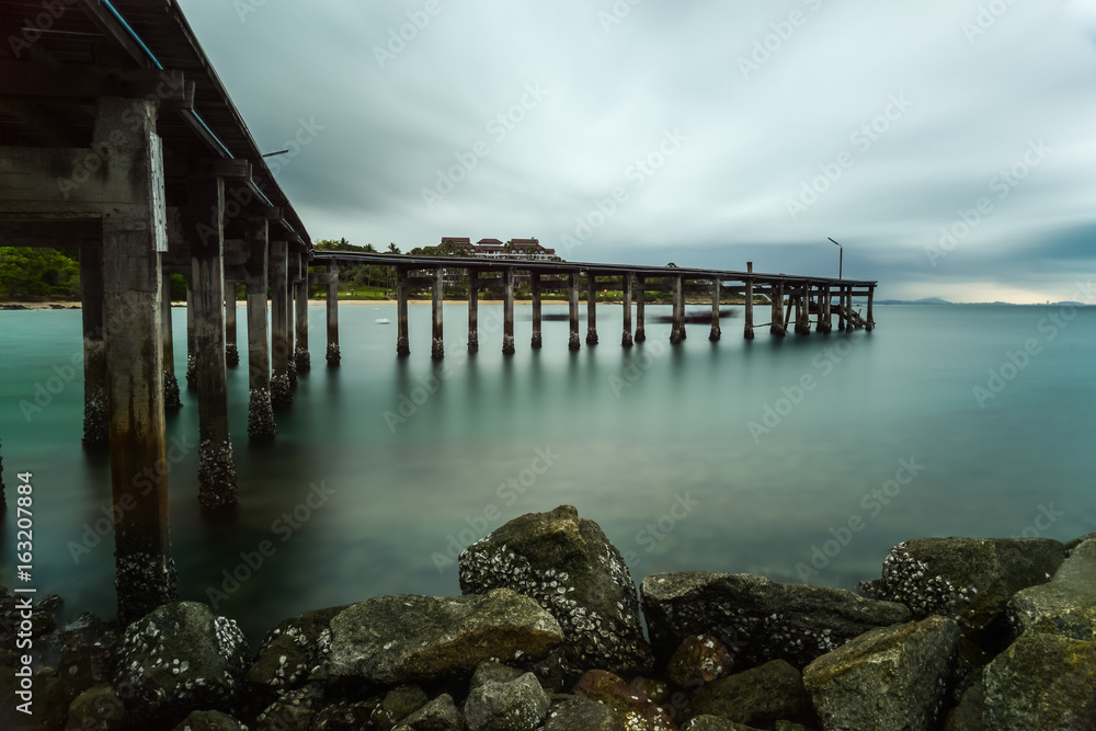Wooden bridge on silky sea with silky rain clouds