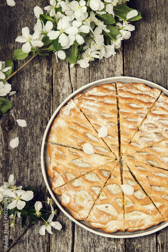 Fototapeta Naklejka Na Ścianę i Meble -  Apple pie, cake sliced on vintage rustic wooden table, decorated flowering branches apple tree. Top view. Selective focus