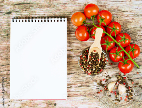 Horizontal food banner with cherry tomatoes, garlic, peppercorns and notebook on wooden background. Empty space for text.