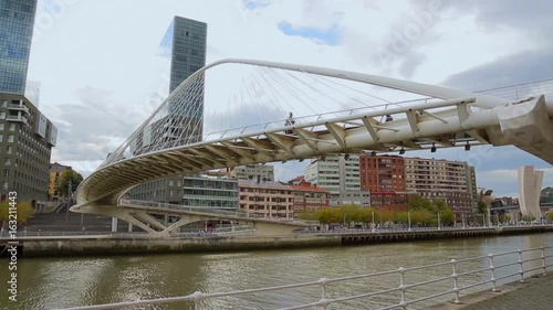 River with footbridge across, shown against city skyline, people along walkway photo