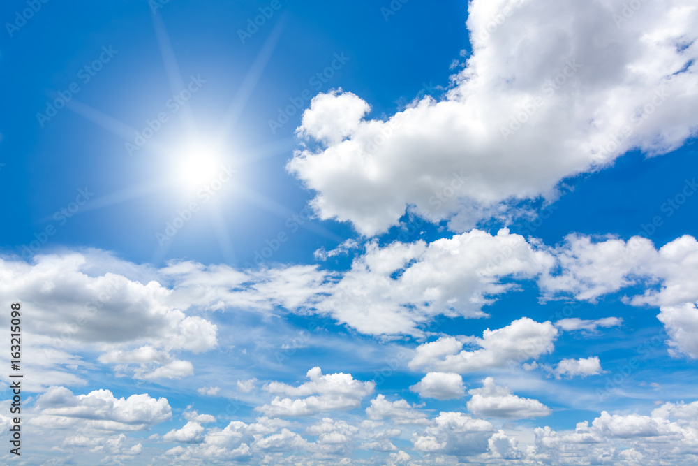 Sun with lens flare in blue sky above clouds.