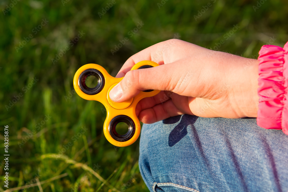 Child holds a fascinating toy spinner in hand on grass background