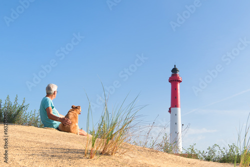 Man and dog sitting near lighthouse at the beach photo