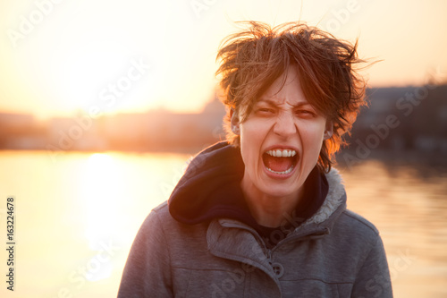 A young woman stands on a city street with a hairy hairdo and screams in hysterics against the backdrop of the rising sun.