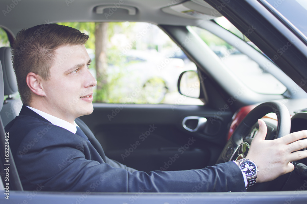 Young and well-dressed businessman sitting in his car. Suit and tie businessman driving his car.