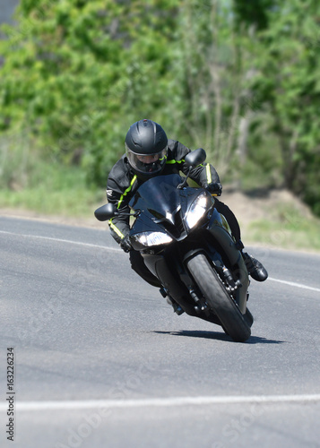 Obraz na płótnie The biker on the black sports motorcycle on a bend on speed w salonie