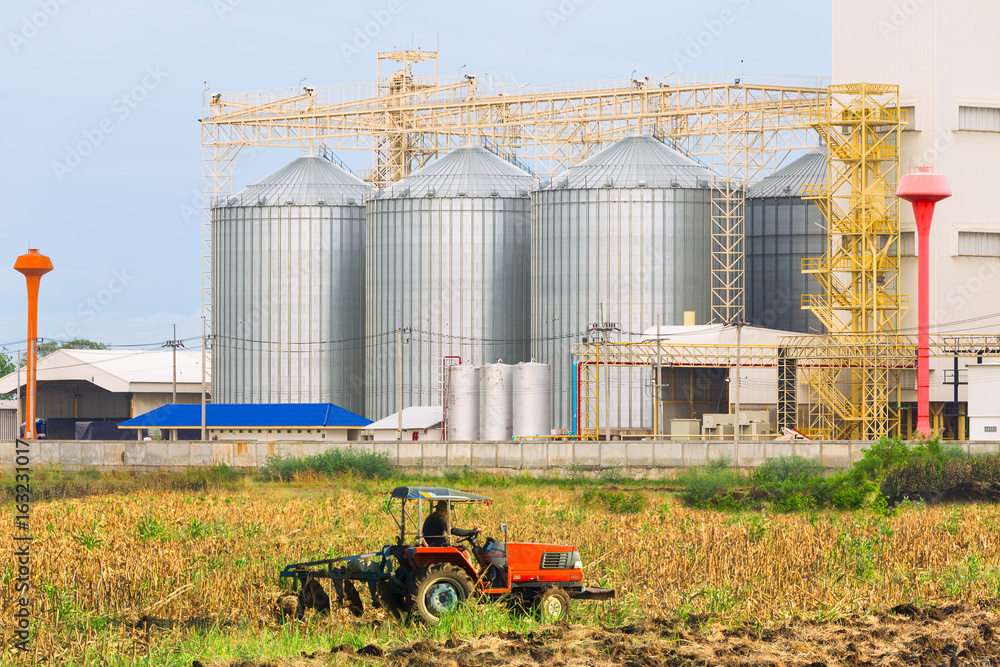 Fototapeta premium Agricultural Silos - Building Exterior, Storage and drying of grains, wheat, corn, soy, sunflower against the blue sky with farm tractors in the foreground.