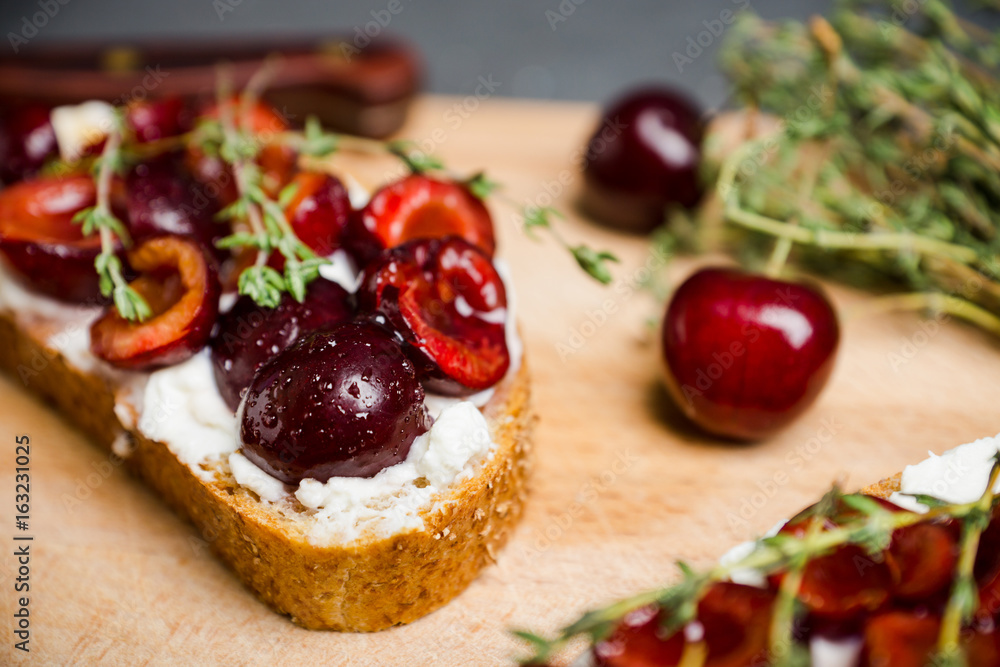 Bread with ricotta cheese and cherries on the wooden background. Shallow depth of field.