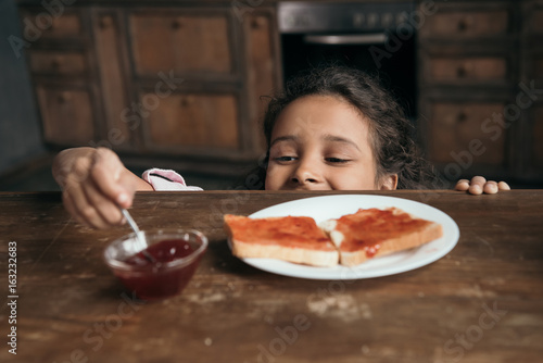 partial view of little girl looking at jam in bowl on table